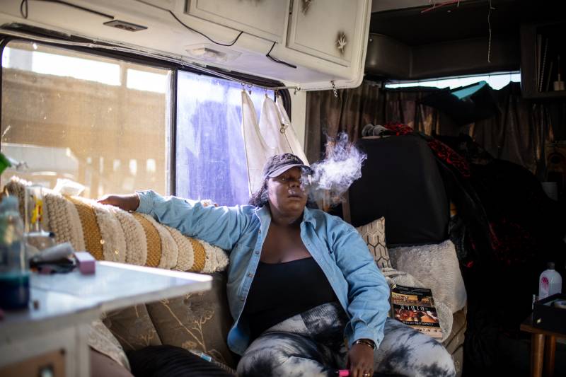 An African American woman wearing a blue denim jacket smoking while seated inside an RV.