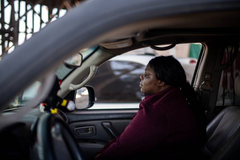 An African American woman looks out pensively from the passenger seat of a car.