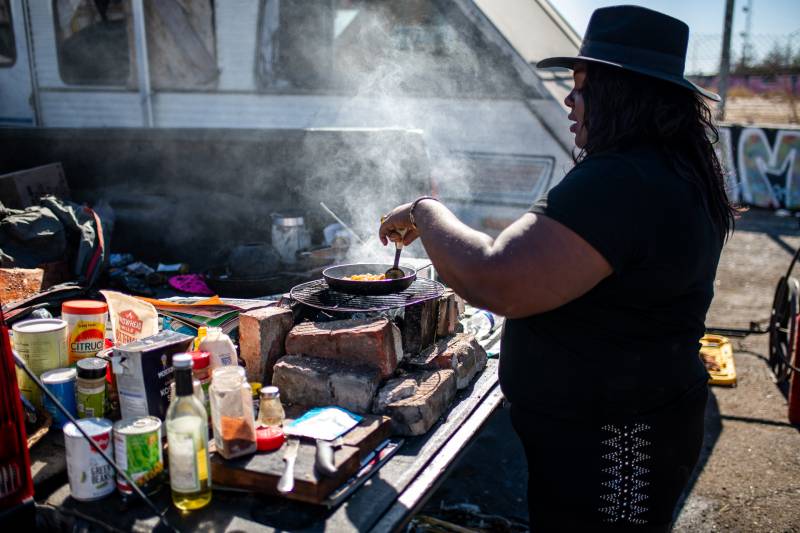 An African American woman cooking food on a BBQ, wearing a broadbrimmed hat.