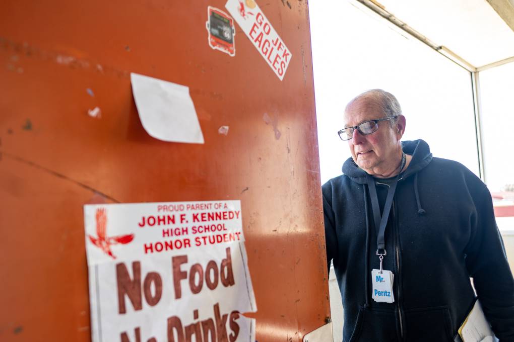 A white man with glasses in a black hoodie stands on the side of the door with a sign that reads "No Food No Drinks."