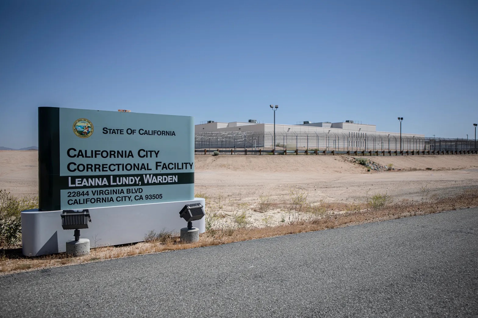the exterior of a prison fence, with a sign that says California City Correctional Facility