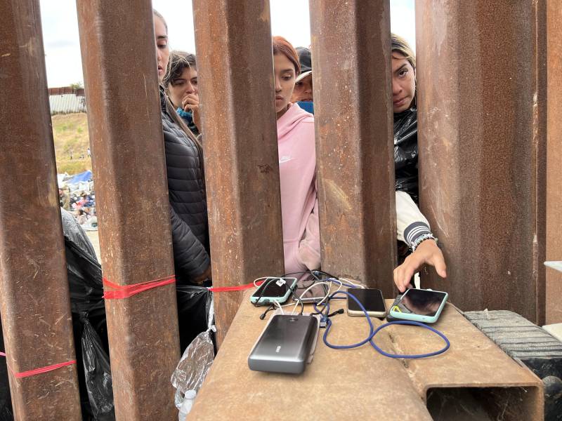 Young woman reach through think metal bars to place and charge their cellphones.