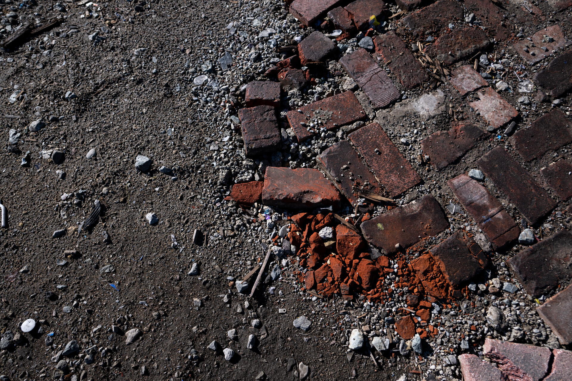A closeup shot of a dirt field with red bricks from a former patio pictured. Everything is burned.