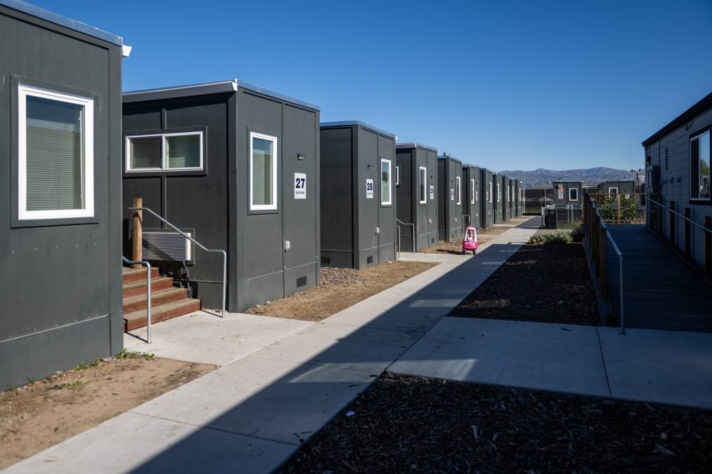 Neat rows of gray shipping containers have been converted into housing. A kid's Little Tikes car in yellow and red is seen on the sidewalk in the distance.