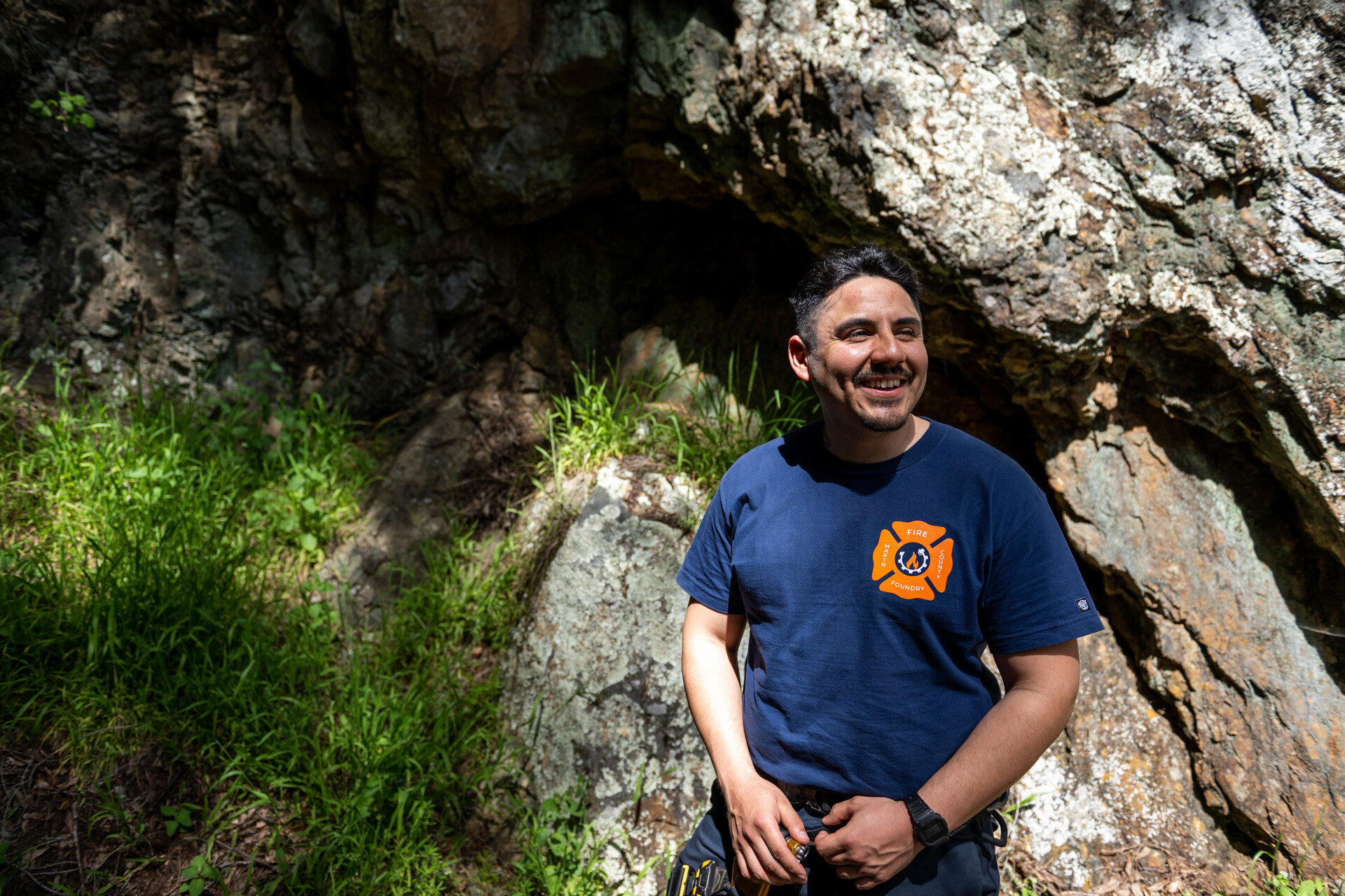A Latino man with a blue tshirt with a FIRE Foundry logo smiles as he looks away from the camera.