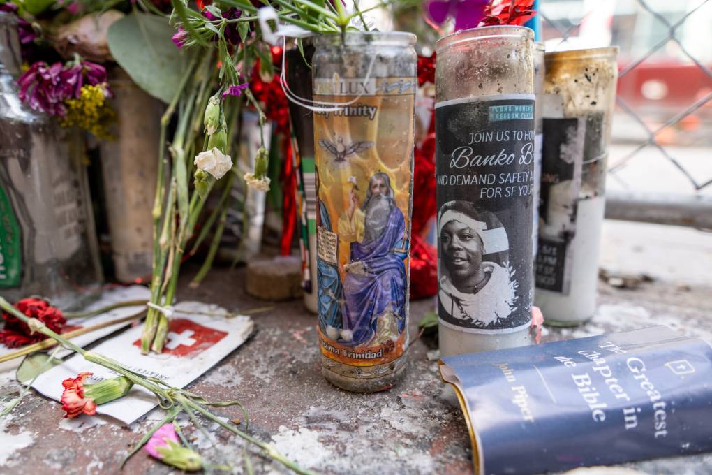 A memorial with flowers, photos and candles on a sidewalk.