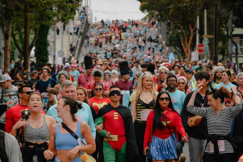 A crowd of people, many in costumes, descend a hilly street in San Francisco.