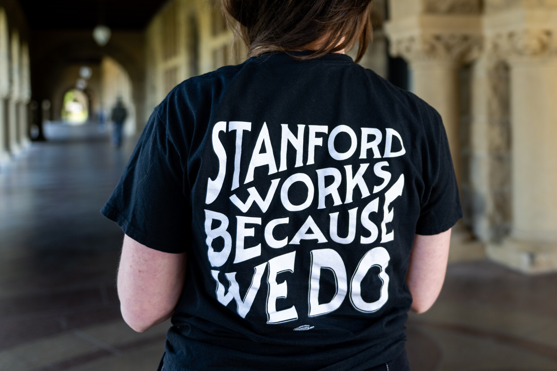 A shot of the back of a woman's black T-shirt that reads, "Stanford works because we do."