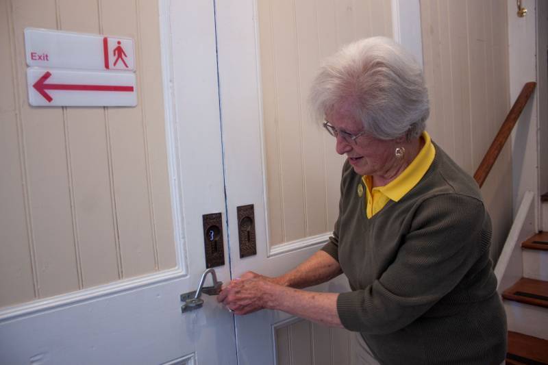 An older woman with white hair unlatches a pair of sliding doors.