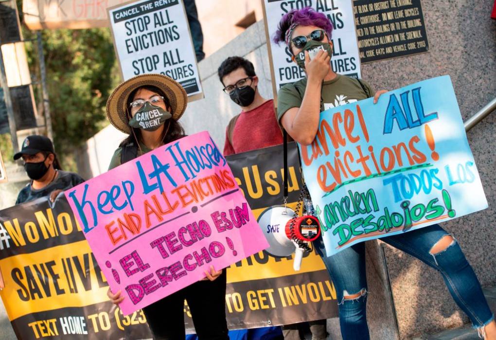 Four people wearing masks and glasses holding colorful signs that read "End all evictions" in English and Spanish.
