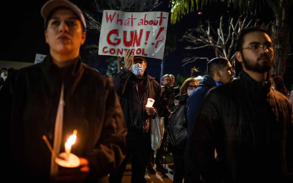 Protest participants stand around some holding candles. One person holds up a poster that reads, 'What about gun control?"