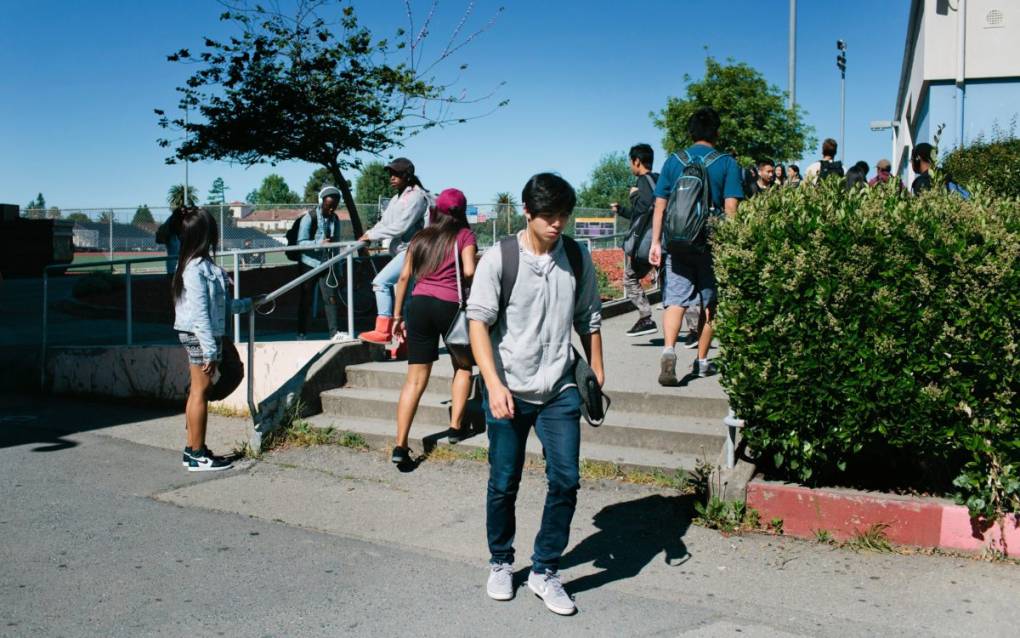 A handful of teenagers of different ethnicities are walking up a small set of concrete stairs, with a couple of them walking down the stairs