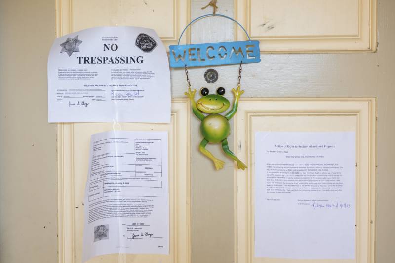 Three papers are taped to a white front door to a home. One reads "No Trespassing" in bold. hanging from the door is an ornament of a green frog and a "Welcome" sign.
