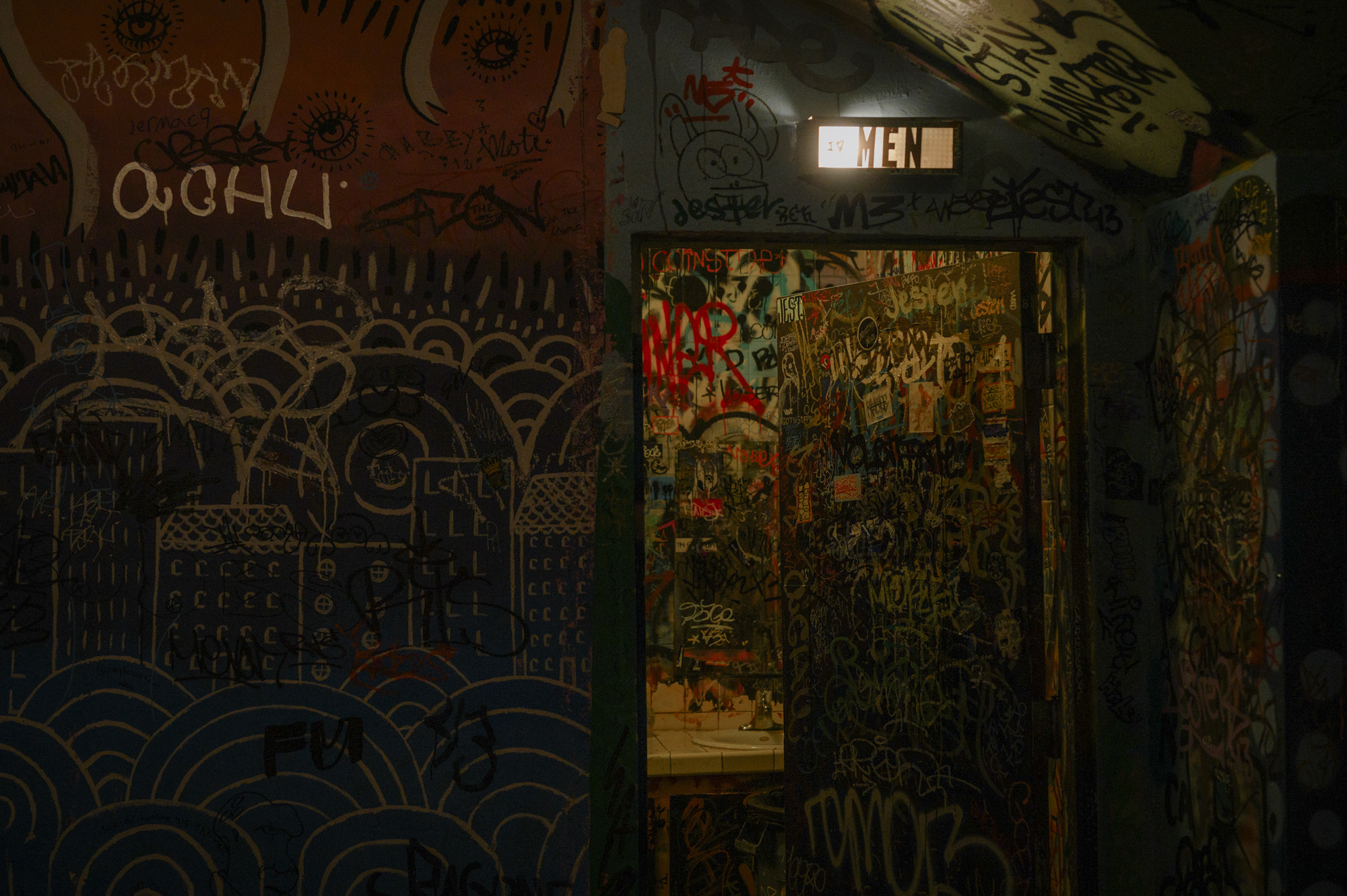 Every inch of the wall outside the men's room is covered with graffiti. As is the door to the men's room, which stands ajar, and so is the wall inside.