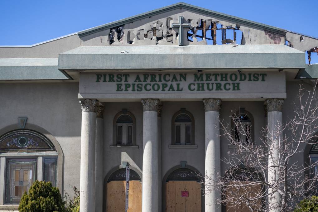 A large columned building with holes in the facade and boarded up doors and a sign reading "First African Methodist Episcopal Church."