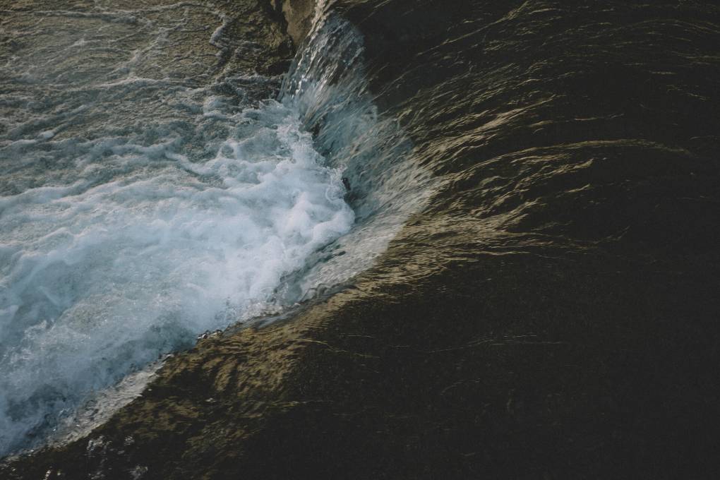A dark-toned image of water in a river rushing over a small rapid