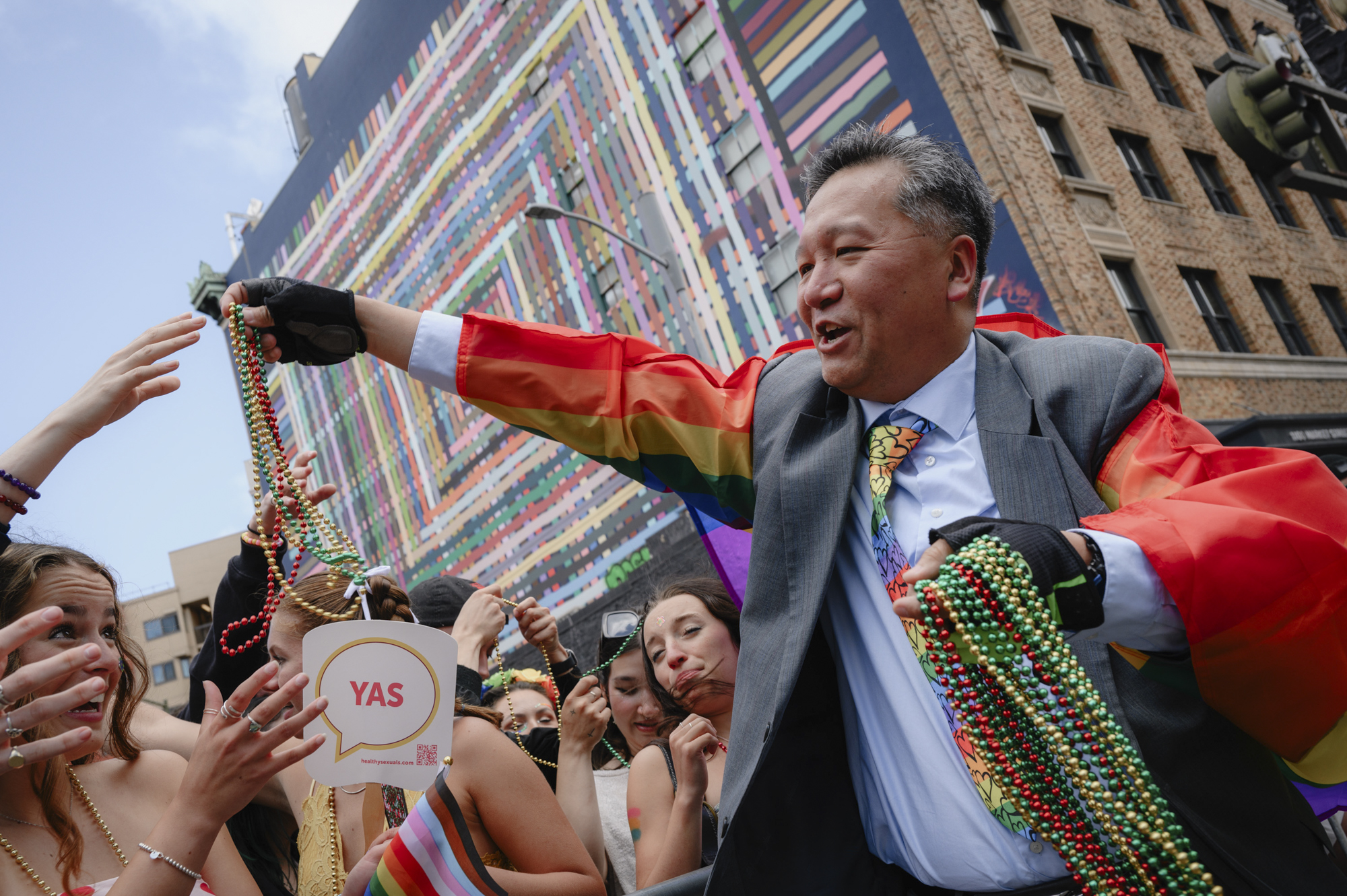 Kit Lem, 47, a legislative aide for San Francisco Supervisor Joel Engardio, hands out bead necklaces as the Pride parade passes down Market Street in downtown San Francisco on June 25, 2023.