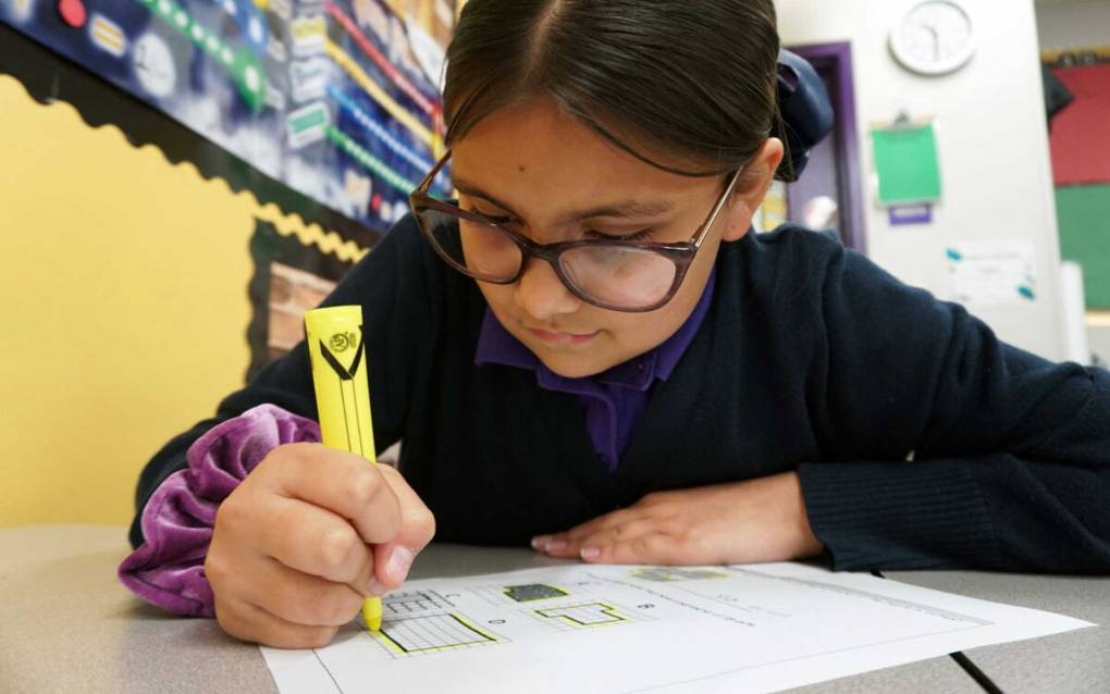 A girl with glasses holding a yellow pen marking up a paper.