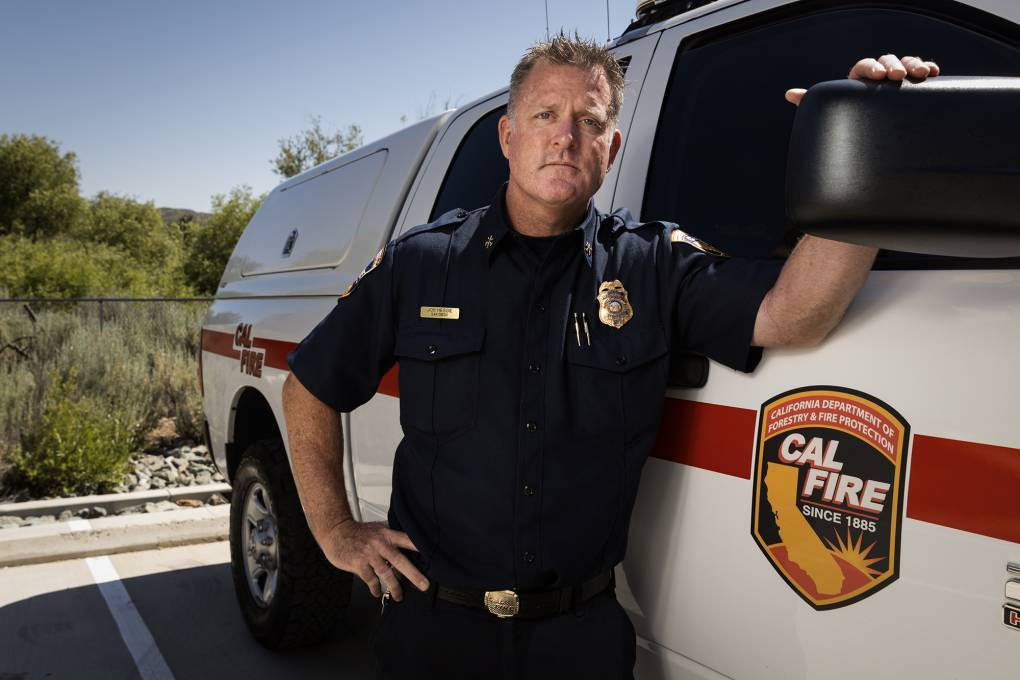 A fire chief in full black uniform stands next to his Cal Fire truck.