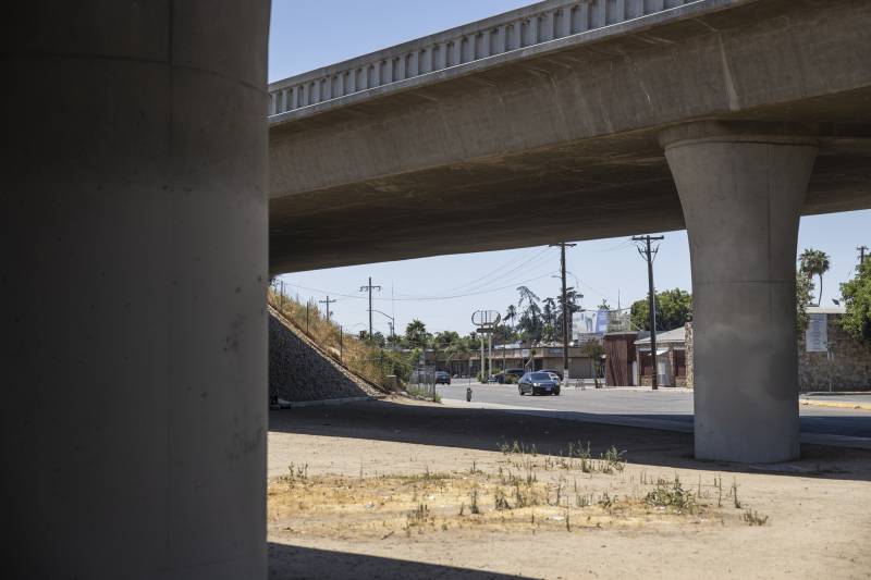 A car drives up a street set below a freeway overpass.