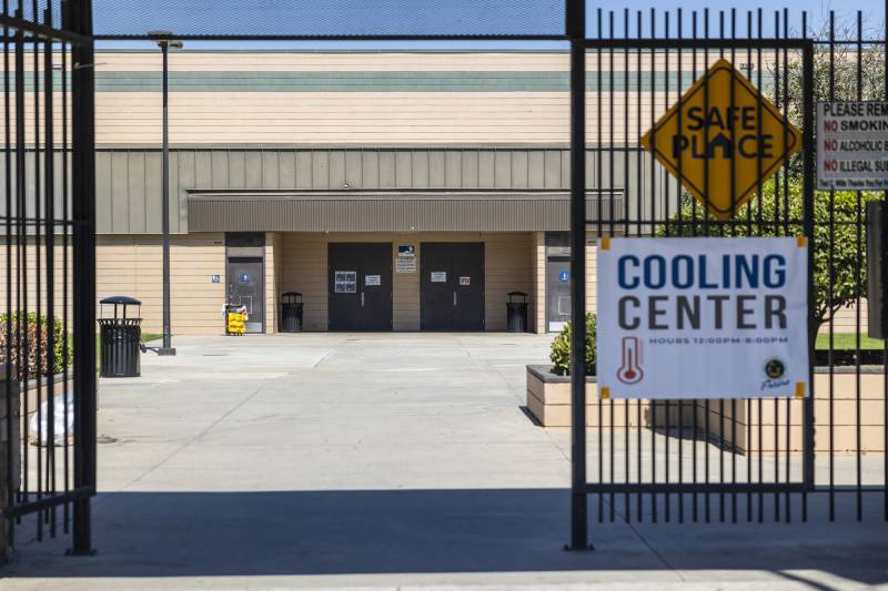 The doors of a large community center are seen beyond a gate with a sign reading "cooling center."