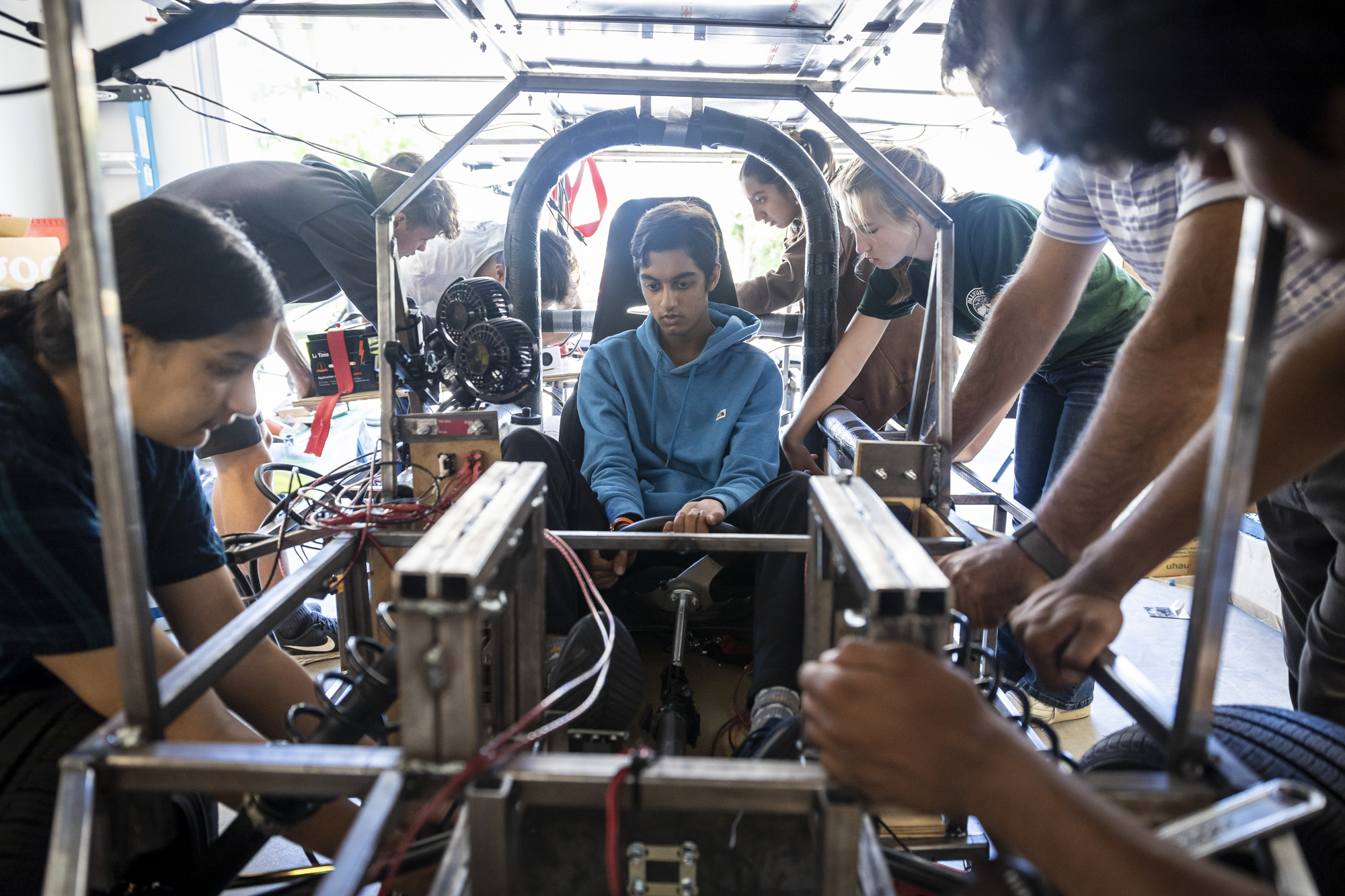An East Indian high school student sits in the middle of a metallic frame as other students work around him.