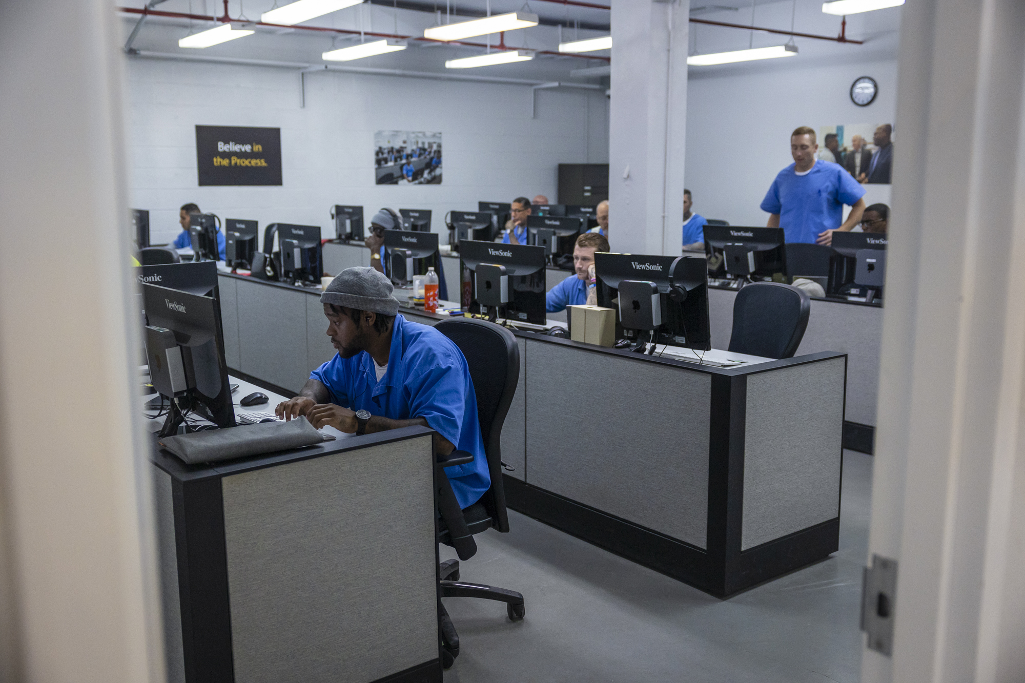 A room full of men sitting at computers and working in blue uniforms.