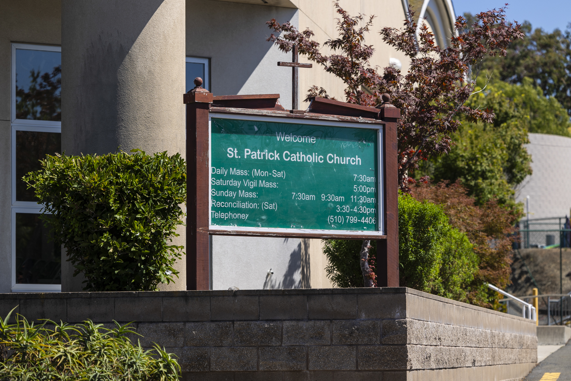 A wooden sign outside a large building that reads "Welcome: St. Patrick Catholic Church" and listing the times of services.