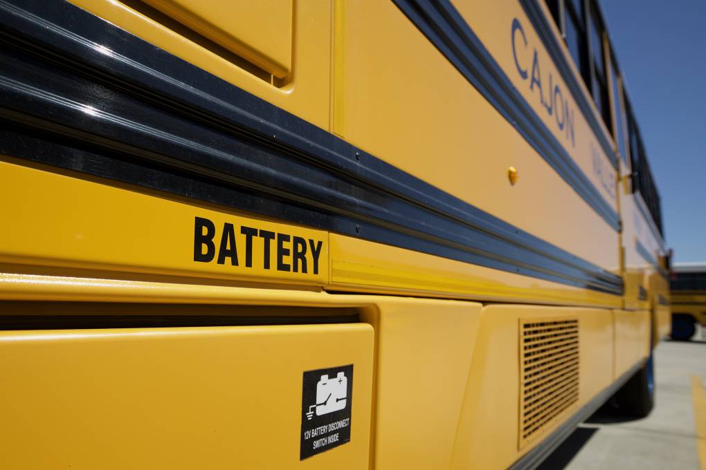 A close-up shot of an electric-powered school bus outside of Cajon Valley Union School District. The word "Battery" is seen above the bus's electric battery storage.