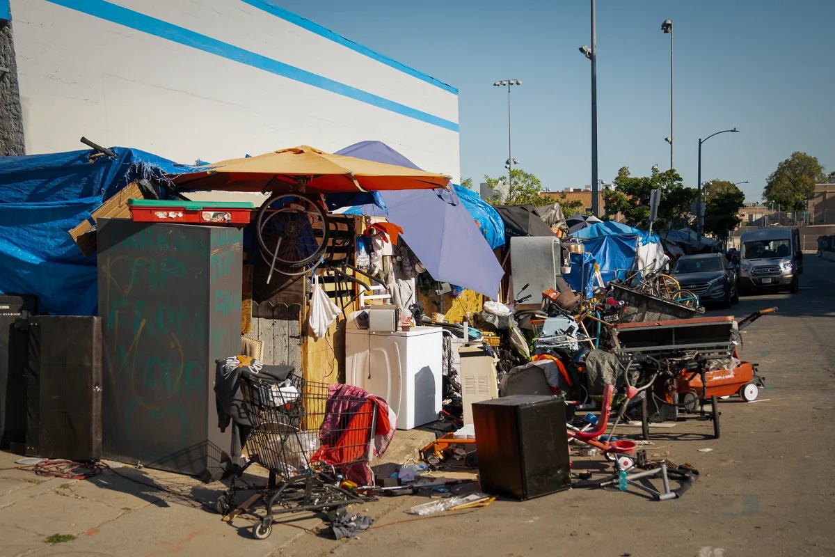 There are tents, belongings scattered and stacked, RVs in the background, a random shopping cart, and more. Many blue tarps cover the tops of the encampment area.