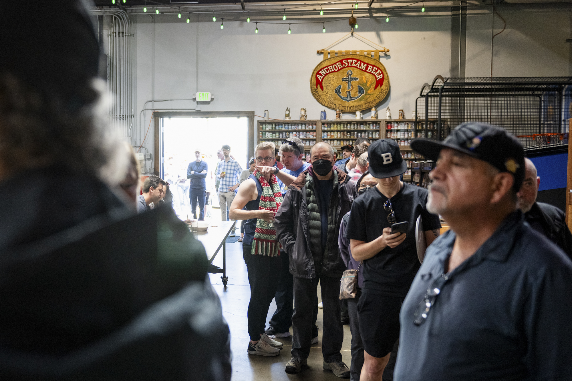 People stand in a line inside a large indoor space with a banner on the wall reading "Anchor Steam Beer."