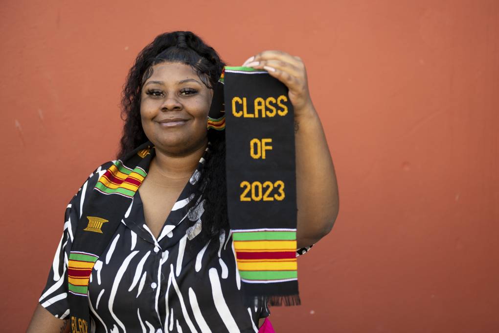 A person holds out a black, green, yellow and red striped graduation stole with the words "Class of 2023" written on it.