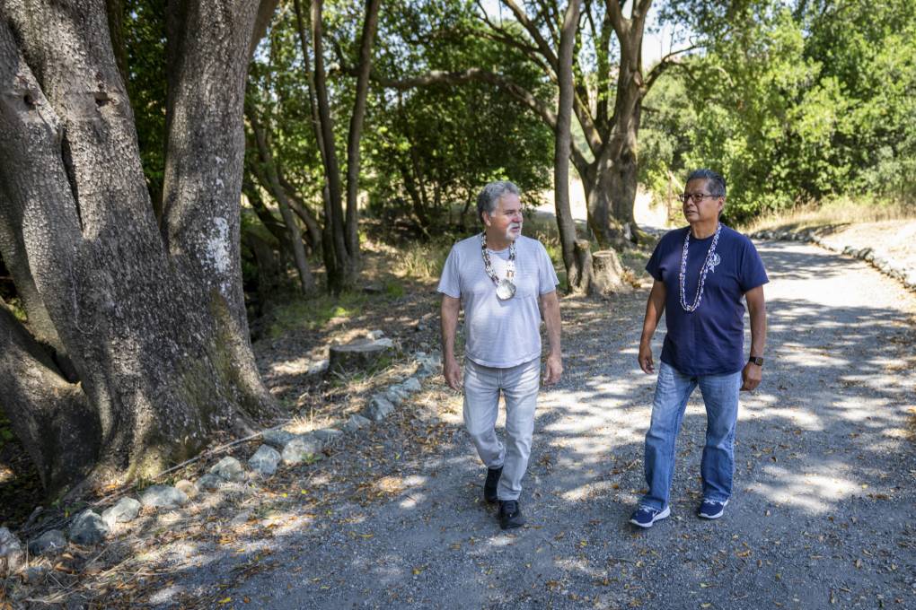 Two people wearing necklaces walk on an outdoor trail.