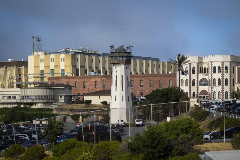 A large walled series of buildings, a guard tower and dozens of parked cars.