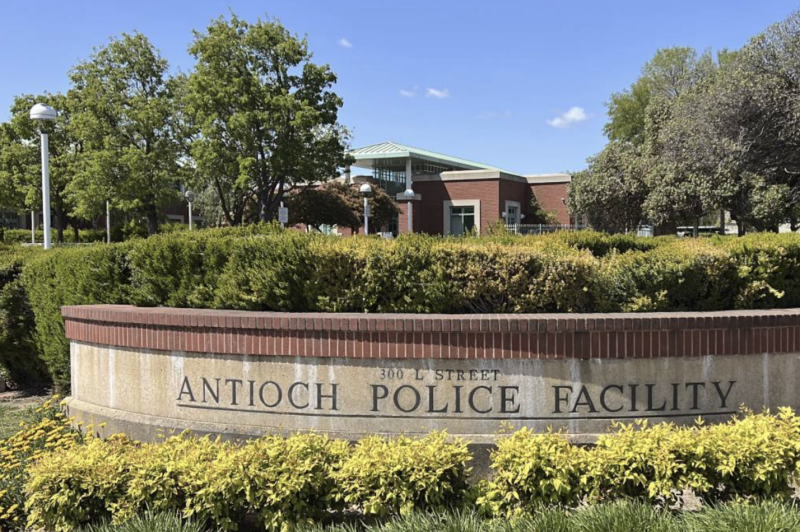A sign carved into stone reads "Antioch Police Facility" with a vegetations and a building in the background.