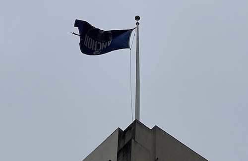 a flag, that says Anchor, is upside down on a pole above a building