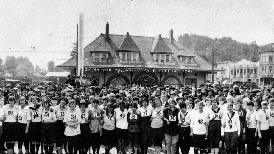 an older black and white photo shows a crowd of women dressed in old-fashioned athlete gear gathered at a start line