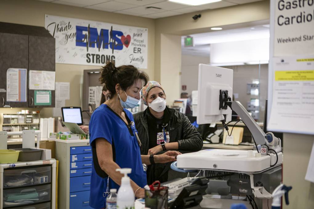 Two women in blue scrubs stand in a hospital.