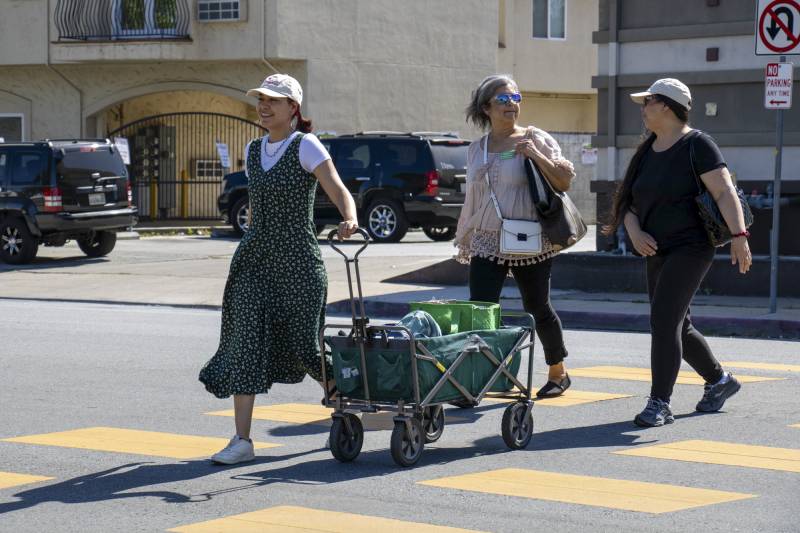 Three people walk across a street as one of them pulls a wagon.