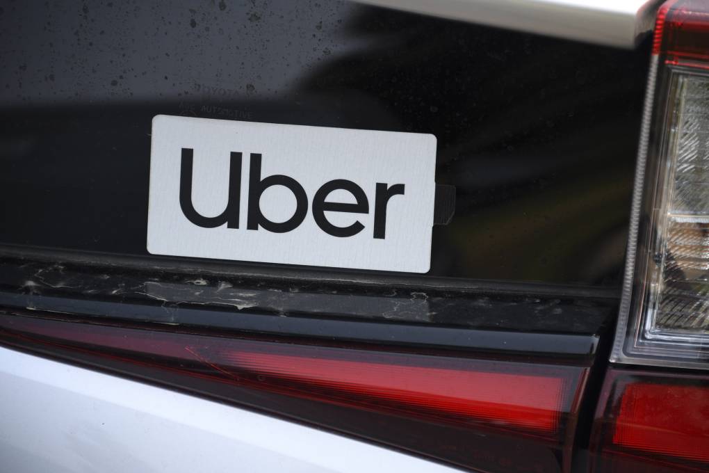 A white bumpersticker with the word "Uber" written on it on a car bumper.