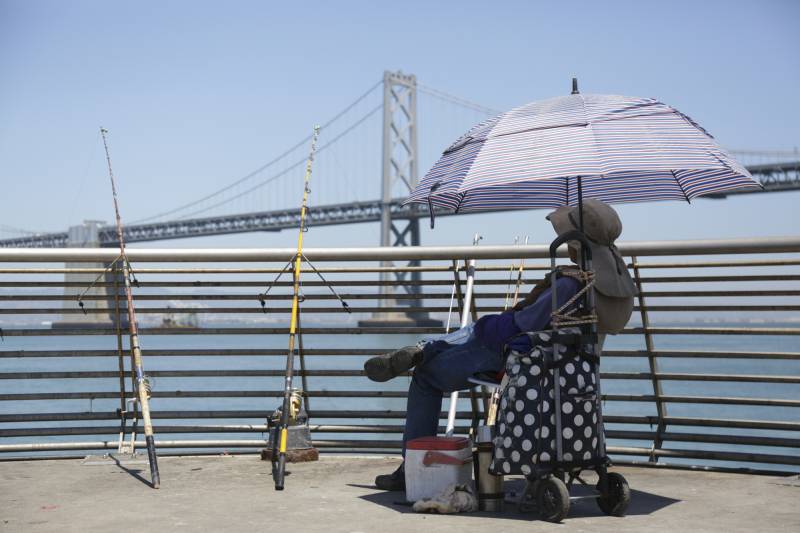 A fisherman waits under the shade of his umbrella in front of the Bay Bridge.