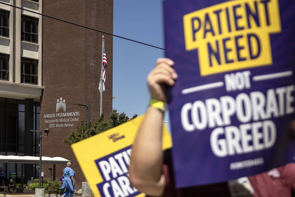A close-up shot of a protestor's sign that reads, "Patient Need Not Corporate Greed" in front of a Kaiser Permanente building in Sacramento, California.