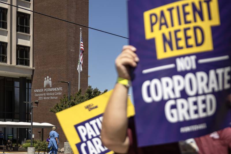 A close-up shot of a protestor's sign that reads, "Patient Need Not Corporate Greed" in front of a Kaiser Permanente building in Sacramento, California.