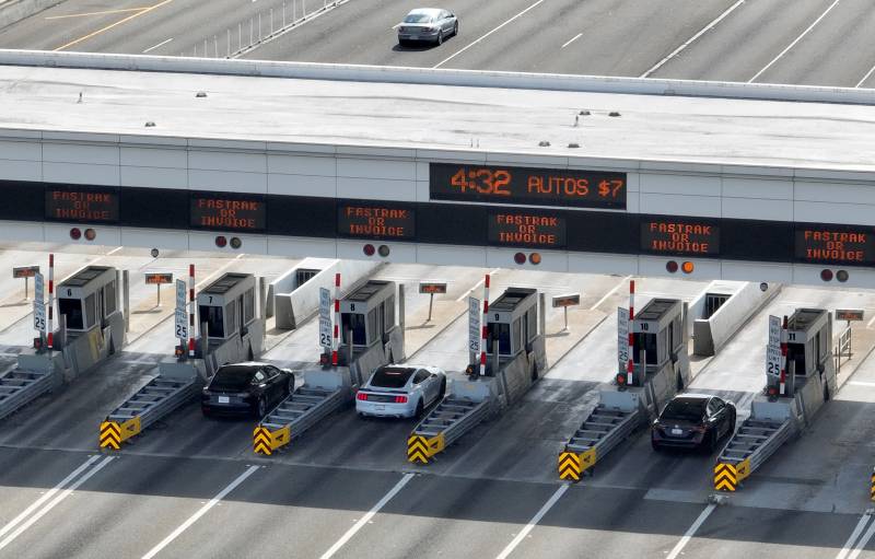 Aerial shot of cars at a series of toll booths on a bridge, with a $7 toll fee in a digital sign above the booths.