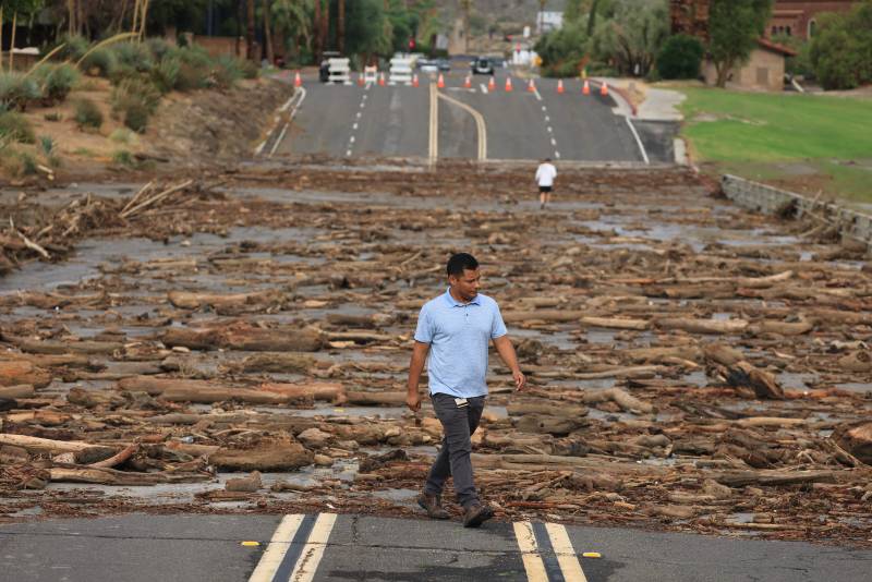 A man walks next to a large highway that has been completely blockaded by debris.