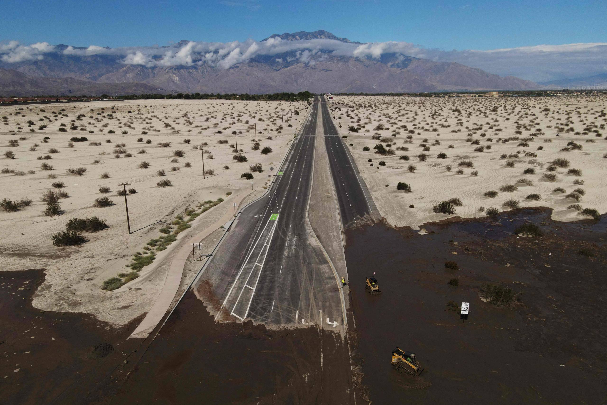 A large freeway cuts through the desert landscape. However, parts of this road are completely blocked off by large quantities of water that remain after heavy rains.