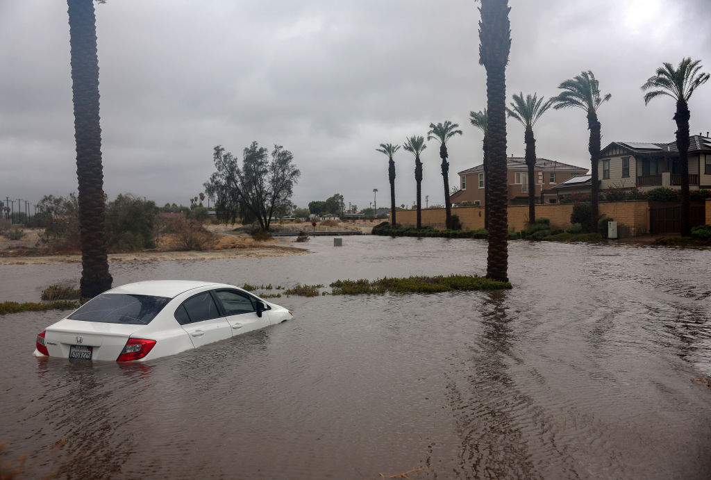A submerged car in a flooded street with houses on a stormy day.