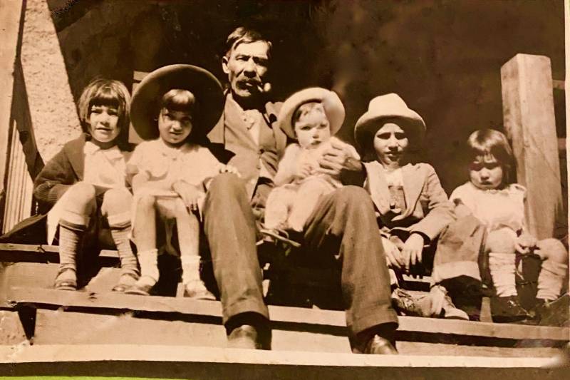 A vintage photo of a man sitting on stairs with five small children, including on on his lap.