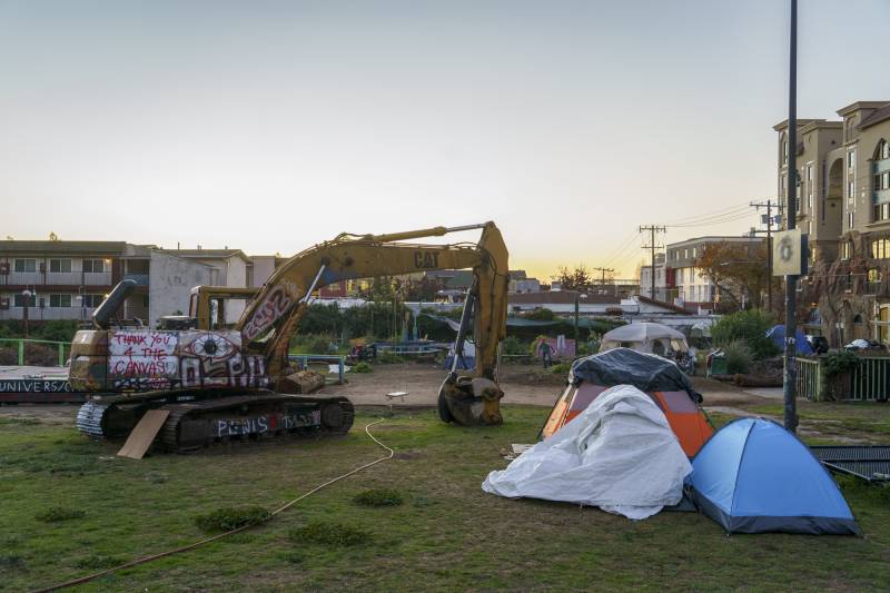 A large open outdoor space with an excavator and some tents in it.