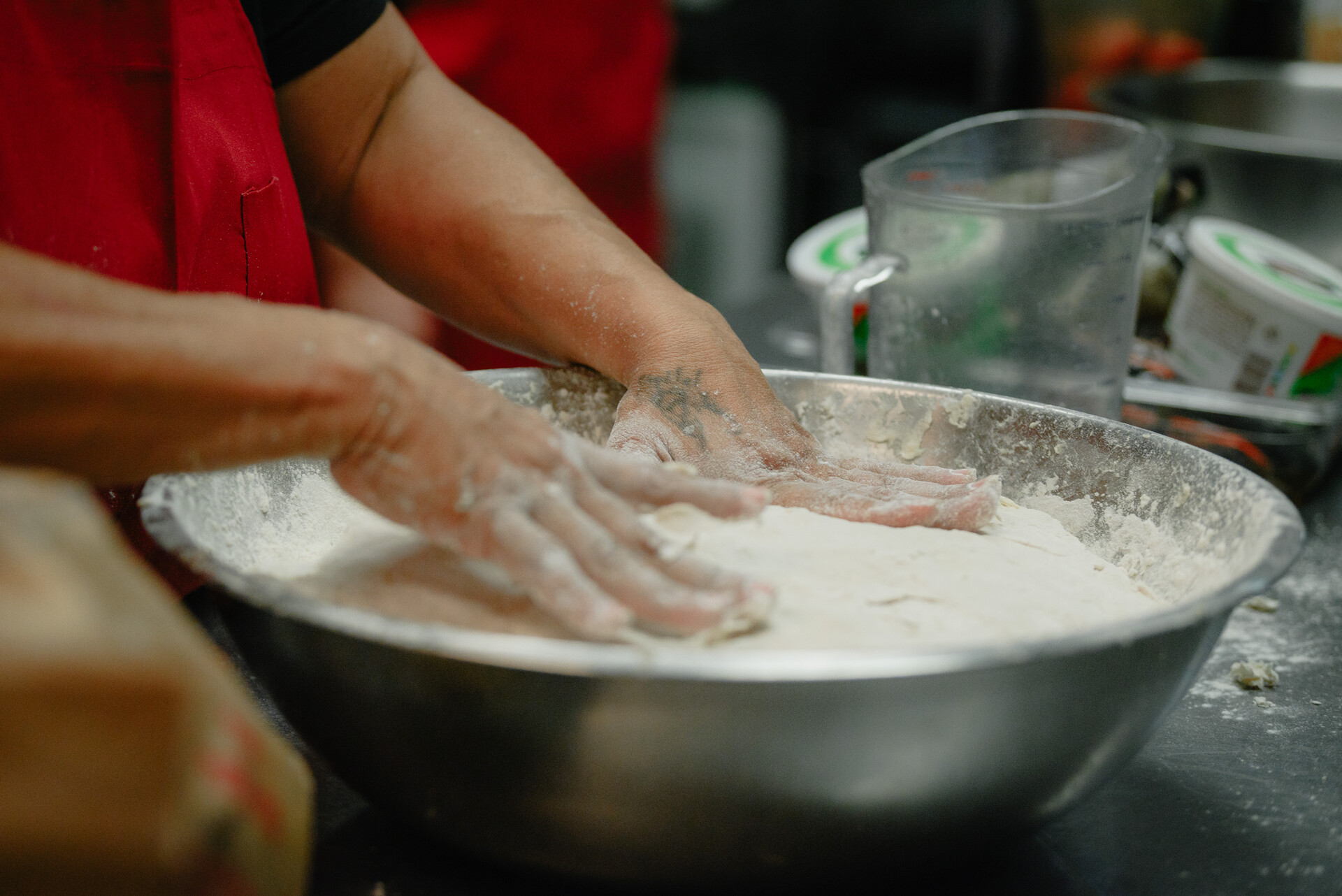 A close-up shot of hands kneading dough in a large, metal bowl. Flour is dusted all over the countertop.
